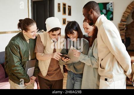Jeune femme souriante montrant quelque chose sur un téléphone portable à ses camarades de classe lorsqu'ils sont debout dans la salle de classe Banque D'Images