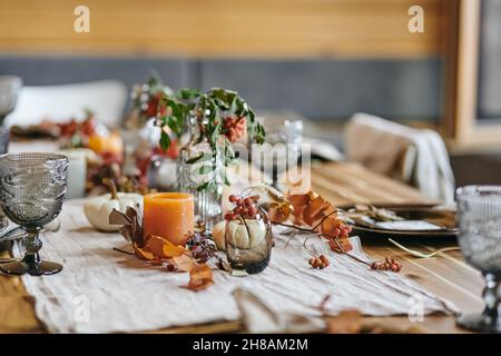 La vie des feuilles d'automne dans un vase et une bouteille sur une table festive servi avec des verres et des ustensiles de cuisine pour un dîner en famille Banque D'Images