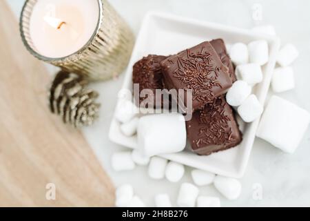 Petits fours au chocolat noir sur fond blanc avec guimauves, pose de bougies plates Banque D'Images