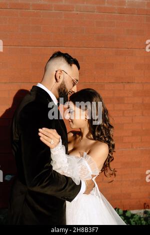 Mariée et marié embrassant contre le mur de brique Banque D'Images