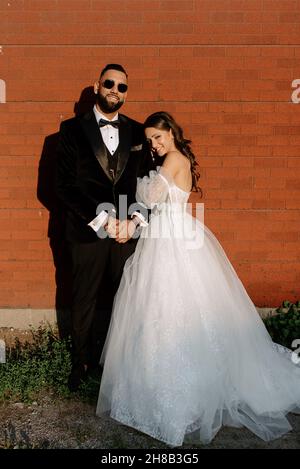 Portrait de la mariée et du marié debout contre le mur de brique Banque D'Images