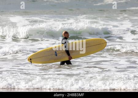 Surfeur mâle d'âge moyen en combinaison transportant sa planche de surf dans l'océan à Palm Beach, Sydney, Australie Banque D'Images