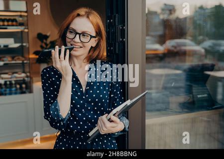 Une femme indépendante se tient à l'extérieur avec un téléphone mobile et utilise un système de reconnaissance vocale sur un smartphone Banque D'Images