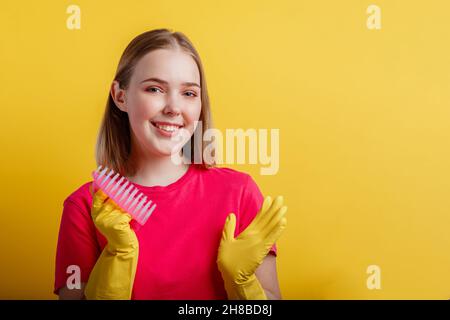 Femme Portrait avec brosse de nettoyage dans des gants en caoutchouc. Jeune blonde heureuse femme souriante prête à nettoyer la maison avec des fournitures de ménage isolées Banque D'Images