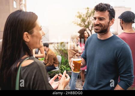 Fête des amis sur le toit - couple parlant ensemble en train de boire des bières sur la terrasse Banque D'Images