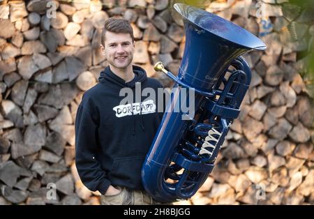 Brackenheim, Allemagne.23 novembre 2021.Micha, de Brackenheim, un musicien portant le nom de scène 'Micha von der Rampe', se dresse devant son tuba bleu devant des billes superposées.Il a raccroché un emploi dans la banque pour sa musique.Au lieu de porter un costume, il porte maintenant un pantalon en cuir et apporte une bouffée d'air frais à la scène pop avec son tuba bleu.(À dpa Un banquier avec un tuba bleu lors d'une visite du village) Credit: Marijan Murat/dpa/Alamy Live News Banque D'Images