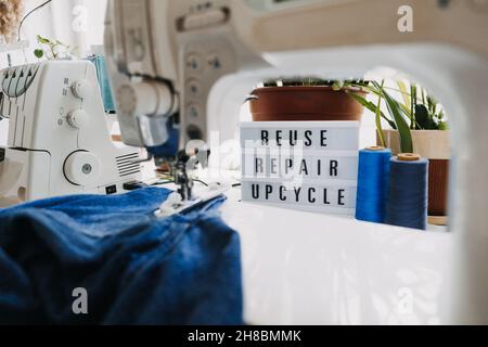 Réutilisation, réparation, mise à niveau du texte sur le panneau lumineux sur l'arrière-plan des machines à coudre.Pile de vieux jeans, de vêtements en denim, de ciseaux, de fils et d'outils de couture Banque D'Images