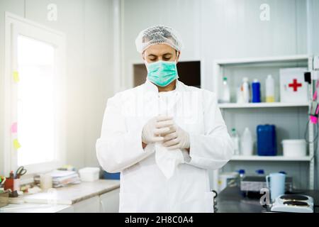 Portrait d'un jeune homme scientifique en blouse de travail, masque, casquette, réalisant une expérience tenant le tissu blanc Banque D'Images