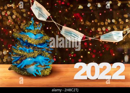 Carte de Noël et du nouvel an 2022.Arbre de Noël fait de gants médicaux bleus, guirlande de masques de protection contre le fond de léguar multicolore Banque D'Images