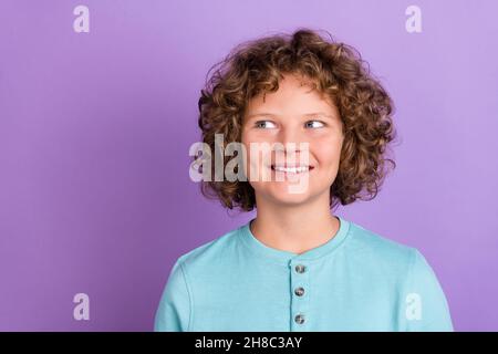 Portrait d'un joli garçon aux cheveux ondulés et gai surpensant l'espace de copie isolé sur fond violet vif de couleur violet Banque D'Images