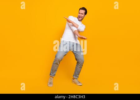 Photo pleine grandeur de brunet impressionné millenny Guy danse vêtements chemise jeans baskets isolées sur fond jaune Banque D'Images