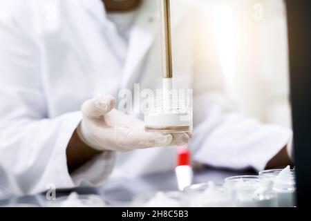 Produit hydratant pour les mains.Ouvrier de laboratoire tenant le verre, le remplir avec la peau de crème hydratante blanche Banque D'Images