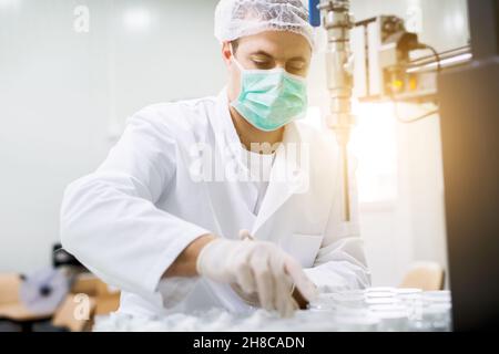 Portrait d'un scientifique masculin en blouse de laboratoire, masque, casquette, réalisant une expérience de travail avec la verrerie Banque D'Images