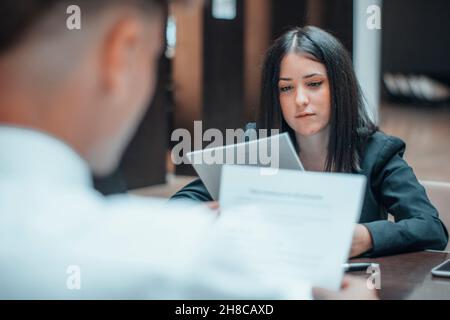 Une jeune femme travaille en équipe avec son client avec des feuilles de papier lors d'une réunion assise Banque D'Images