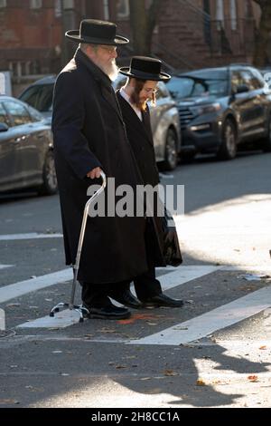 Un juif orthodoxe avec une canne traverse la rue avec son petit-fils le jour de l'automne Banque D'Images