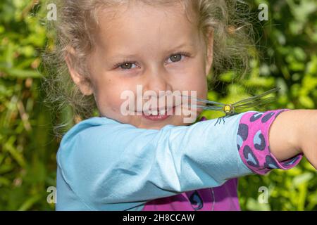 Darner bleu-vert, aeshna du sud, aubérante du sud (Aeshna cyanoa), petite fille souriante avec une libellule de l'aubéenne sur son bras, Allemagne Banque D'Images