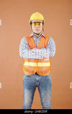 Portrait d'un entrepreneur confiant dans un gilet brillant, des lunettes et un casque de sécurité croisant les bras et regardant la caméra Banque D'Images