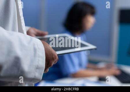 Gros plan du médecin tenant un comprimé moderne pour le diagnostic d'ostéopathie, travaillant tard.Dispositif d'analyse Medic avec image du squelette humain pour les résultats médicaux et de soins de santé.OS à l'écran Banque D'Images