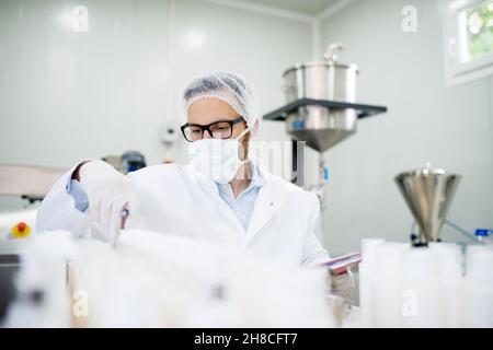 Jeune technologue qui fait des crèmes de soin du visage.Assis dans une usine de produits cosmétiques. Banque D'Images