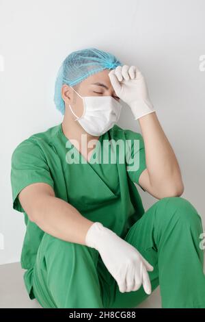 Infirmière masculine stressée et épuisée assise sur le sol dans le couloir de l'hôpital après la chirurgie difficile Banque D'Images