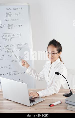Professeur d'université menant la leçon en ligne, parlant dans le microphone et pointant sur le tableau blanc Banque D'Images