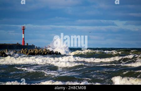 Climat orageux sur la mer, vagues éclaboussant avec mousse, phare rouge et blanc et mouette volante Banque D'Images