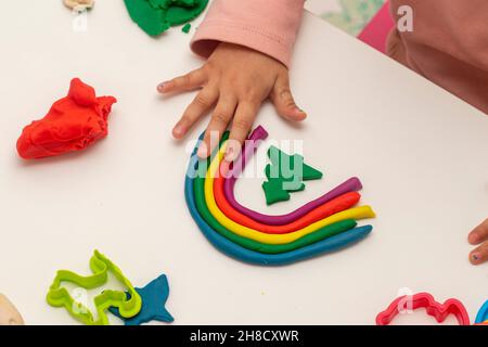 Fille jouant de la pâte.Fille faisant arc-en-ciel avec de la pâte sur fond blanc.Faire différentes formes avec de la pâte. Banque D'Images