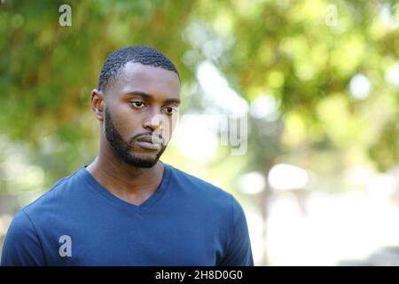 Un homme inquiet avec une peau noire distrait en regardant loin marcher dans un parc Banque D'Images