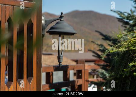 Une lanterne ancienne avec une lampe LED est suspendue sur une clôture en bois devant un sapin, en face des montagnes. Banque D'Images