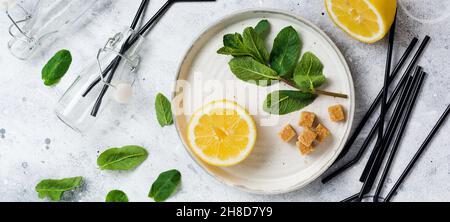 Branche fraîche de menthe, citron et morceaux de sucre de canne sur plaque de céramique sur fond de béton ancien. Banque D'Images