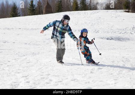 l'enfant apprend à skier avec son père dans les montagnes enneigées par une journée d'hiver froide et ensoleillée.Joies saisonnières, bonne enfance, mode de vie sain.Sports e Banque D'Images