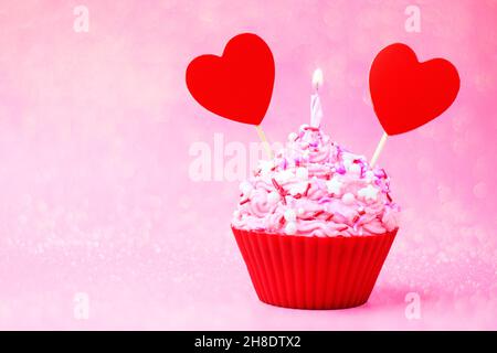 Gâteau de Saint-Valentin.Cupcake à la crème rose et arrosé, avec coeur rouge et sparkler sur fond rose avec bokeh.Carte postale concept à Valent Banque D'Images