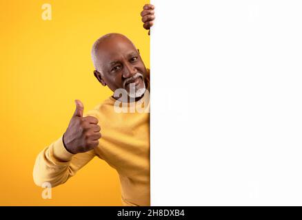 Homme noir souriant avec une bannière vierge en papier blanc montrant le pouce vers le haut, offrant de l'espace pour la publicité, la maquette Banque D'Images