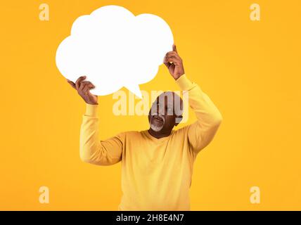 Homme noir âgé tenant une bulle de parole vide avec maquette pour votre annonce sur fond orange studio Banque D'Images