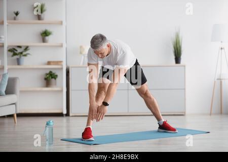 Homme sportif senior qui étire les jambes, s'entraîner à la maison, faire des exercices de flexibilité et mener un style de vie sain, sur toute la longueur Banque D'Images