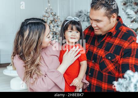 Père de famille asiatique, mère avec fille petite fille célébrant Noël ou nouvel an.Race mixte maman, papa, fille décorant Christa arbre huggi Banque D'Images