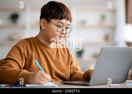 Gros plan sur un adolescent chinois qui fait ses devoirs à l'aide d'un ordinateur portable Banque D'Images