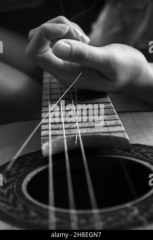 Cordes de guitare brisées avec mains de femmes, réparation de guitare. Image monochrome Banque D'Images