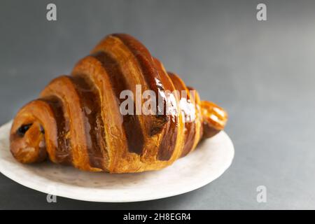 Un croissant français fraîchement préparé avec garniture au chocolat se trouve sur une soucoupe blanche sur une table grise.Concept de boulangerie traditionnelle.Copier l'espace. Banque D'Images