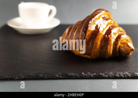 Un croissant français fraîchement préparé avec une garniture au chocolat se trouve sur le tableau d'ardoise avec une tasse de boisson chaude.De délicieuses pâtisseries.Copier l'espace. Banque D'Images