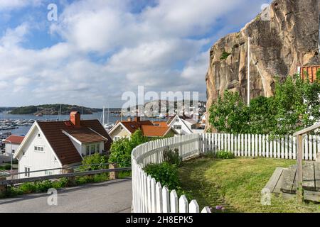 Fjällbacka, Suède -10 juin 2021: Vue de la colline avec clôture blanche incurvée en premier plan, haute roche et bâtiments typiques, mer et baie Banque D'Images