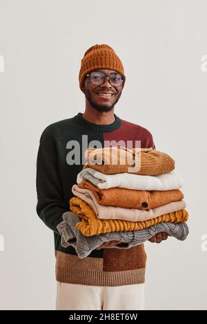 Portrait vertical à la taille du jeune homme afro-américain tenant une pile de chandails tricotés à la main et souriant à l'appareil photo Banque D'Images
