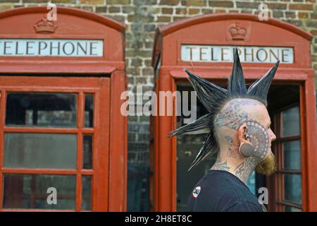 Punk avec la coiffure mohawk devant la boîte téléphonique rouge Banque D'Images