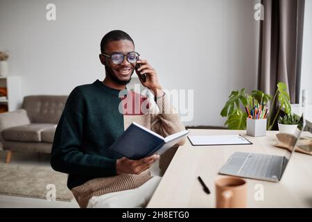 Portrait d'un jeune homme afro-américain portant des lunettes tout en travaillant à la maison et en parlant au smartphone, espace de copie Banque D'Images