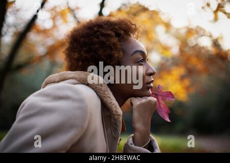 Jeune femme attentionnés avec feuille d'automne rouge dans le parc Banque D'Images