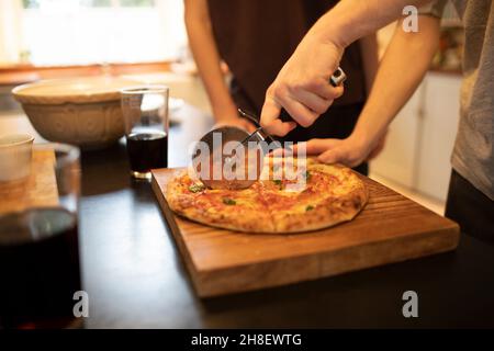 Les garçons trancheuses de pizza maison sur planche à découper dans la cuisine Banque D'Images