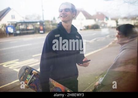 Joyeux adolescent avec smartphone et planche à roulettes à l'arrêt de bus Banque D'Images