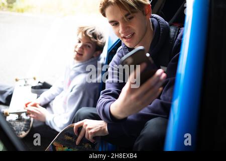 Adolescents avec smartphone et planches à roulettes en voiture Banque D'Images