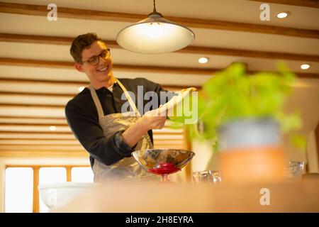 Joyeux jeune homme qui fait de la pâte maison dans la cuisine Banque D'Images