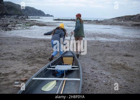 Jeune couple tirant canoë sur la plage, Kent, Royaume-Uni Banque D'Images